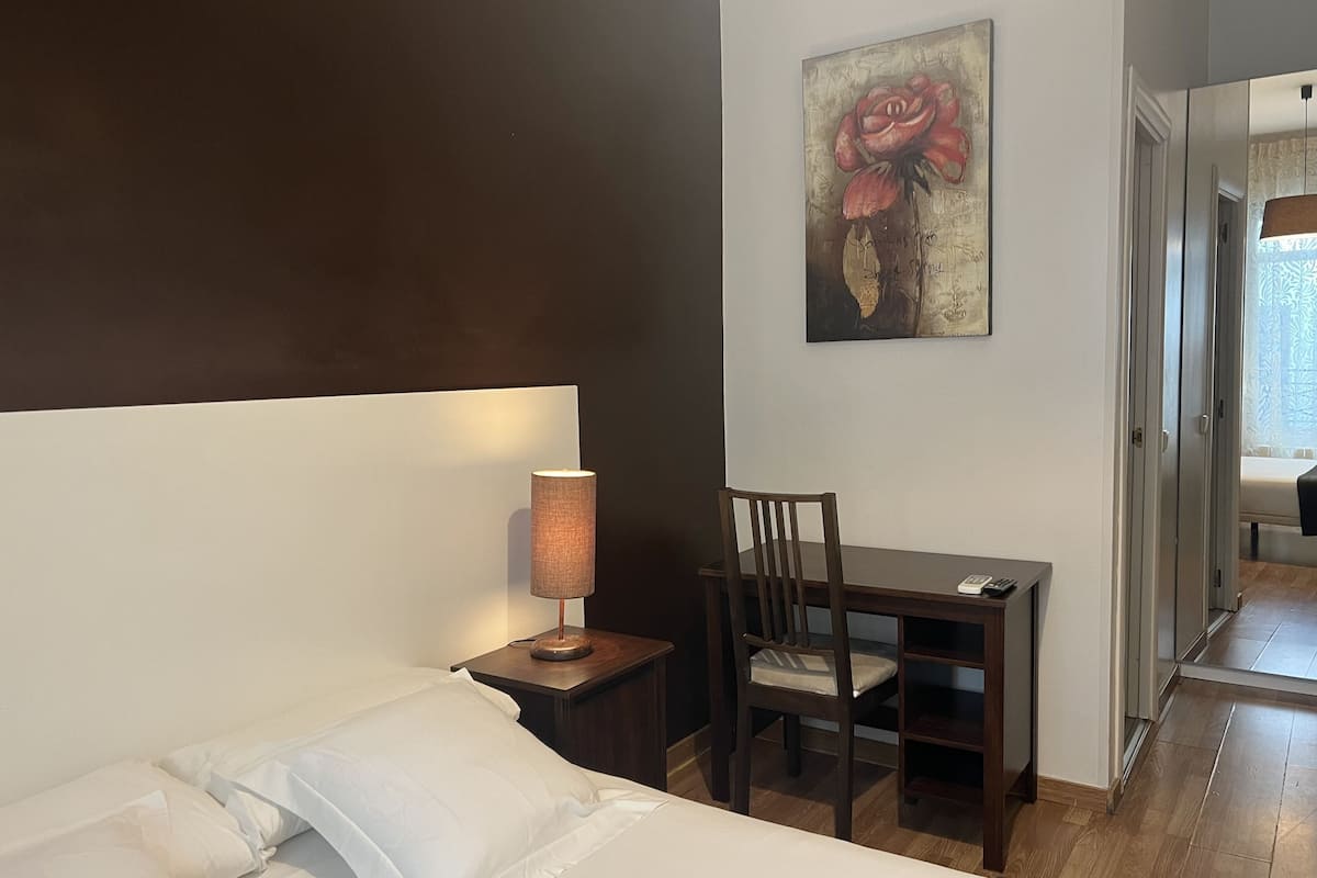 A hotel room with a bed, a desk with a chair, a lamp, and a painting on the wall.