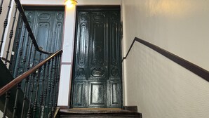 A staircase with wooden steps and black balusters, leading to a dark wooden door with intricate designs. - THC Gran Via Hostel (Madrid)