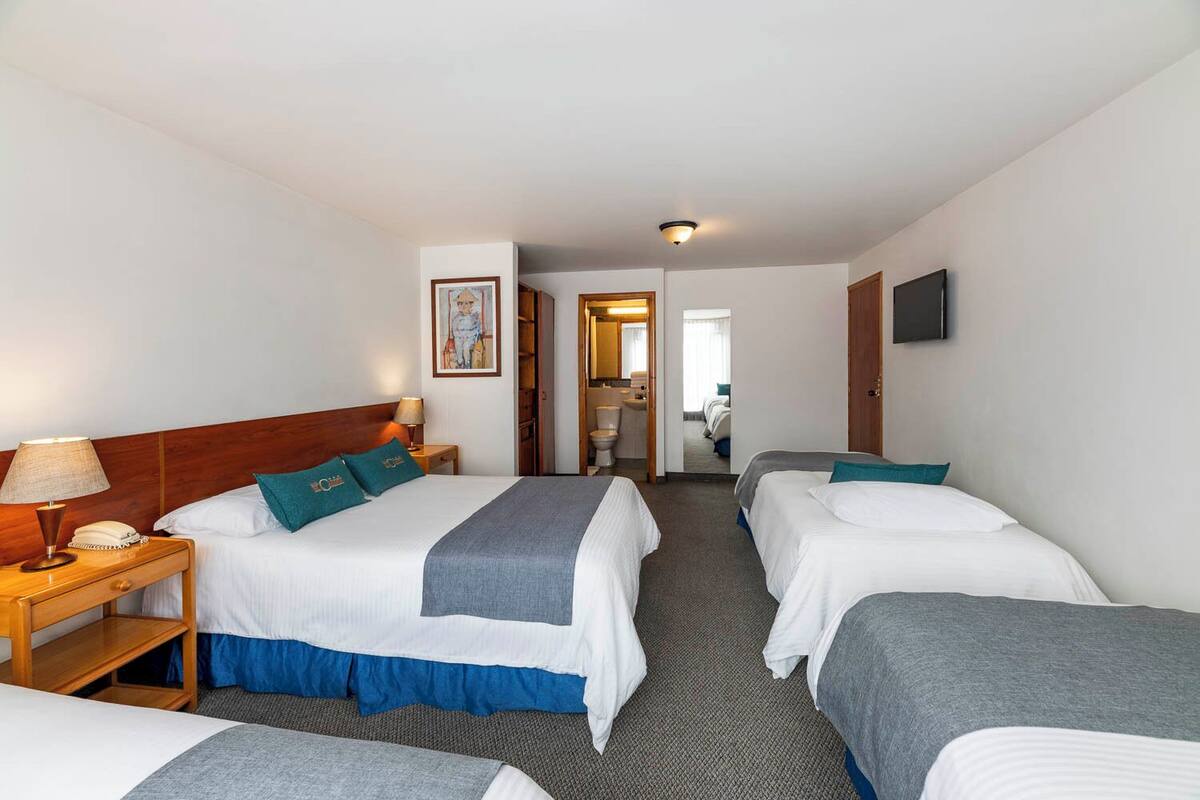 A hotel room with two single beds, a wooden nightstand with a lamp, a telephone, and a framed picture on the wall.