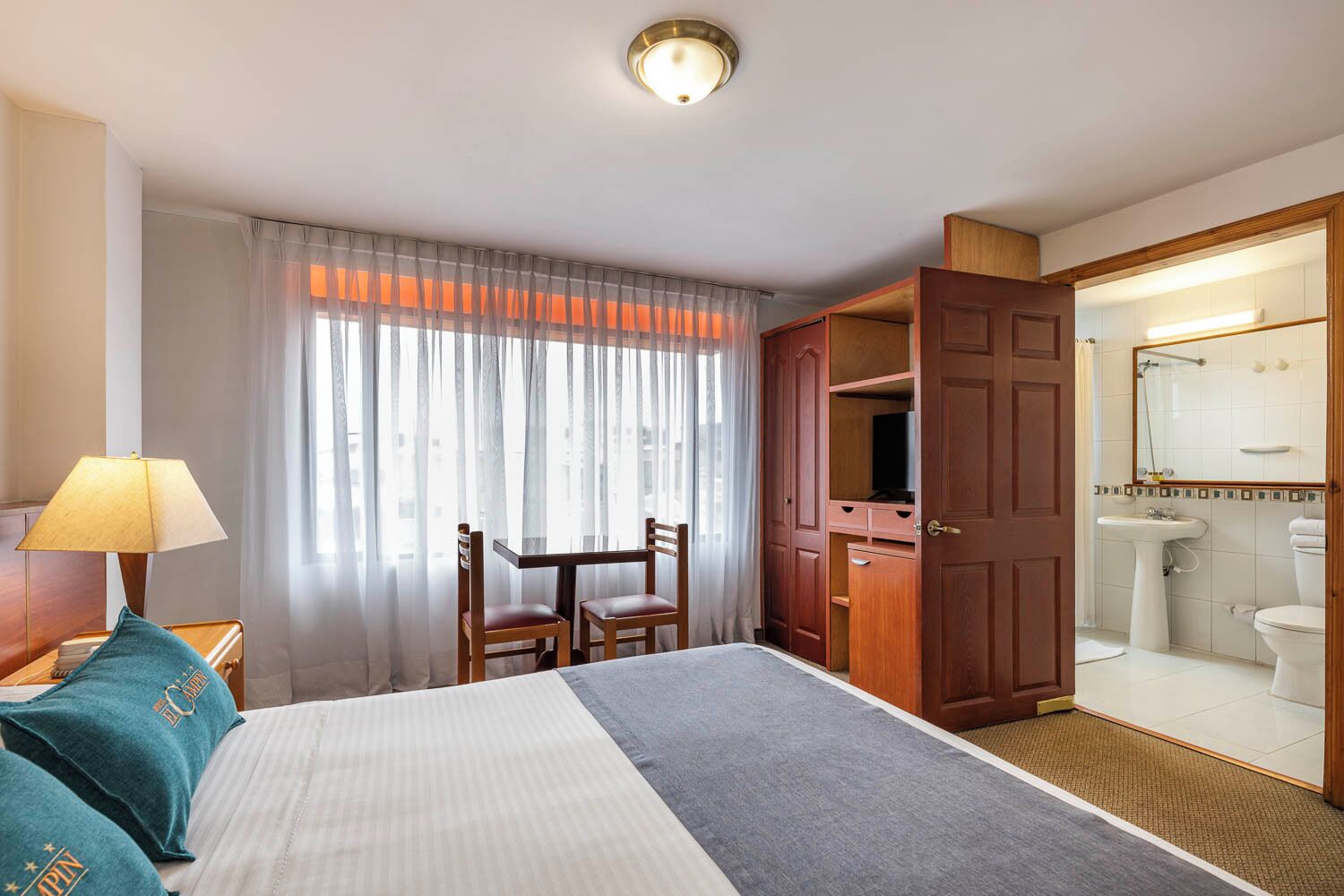 A hotel room with a bed, a desk, a chair, a lamp, a wardrobe, and a bathroom.
