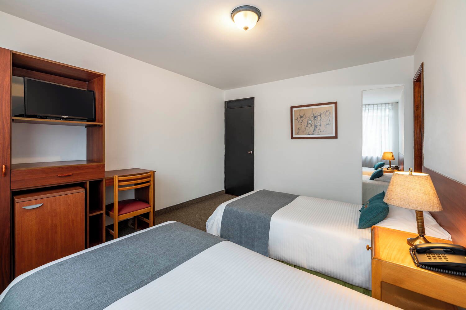 Ein Hotelzimmer mit zwei Betten, einem Schreibtisch, einem Fernseher und einem Spiegel.