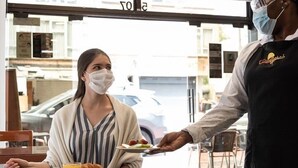 Una persona sirviendo comida a un cliente en un café con vista a la calle.