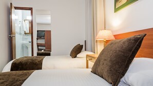 Una habitación de hotel con dos camas, una mesita de noche, una lámpara y un espejo.