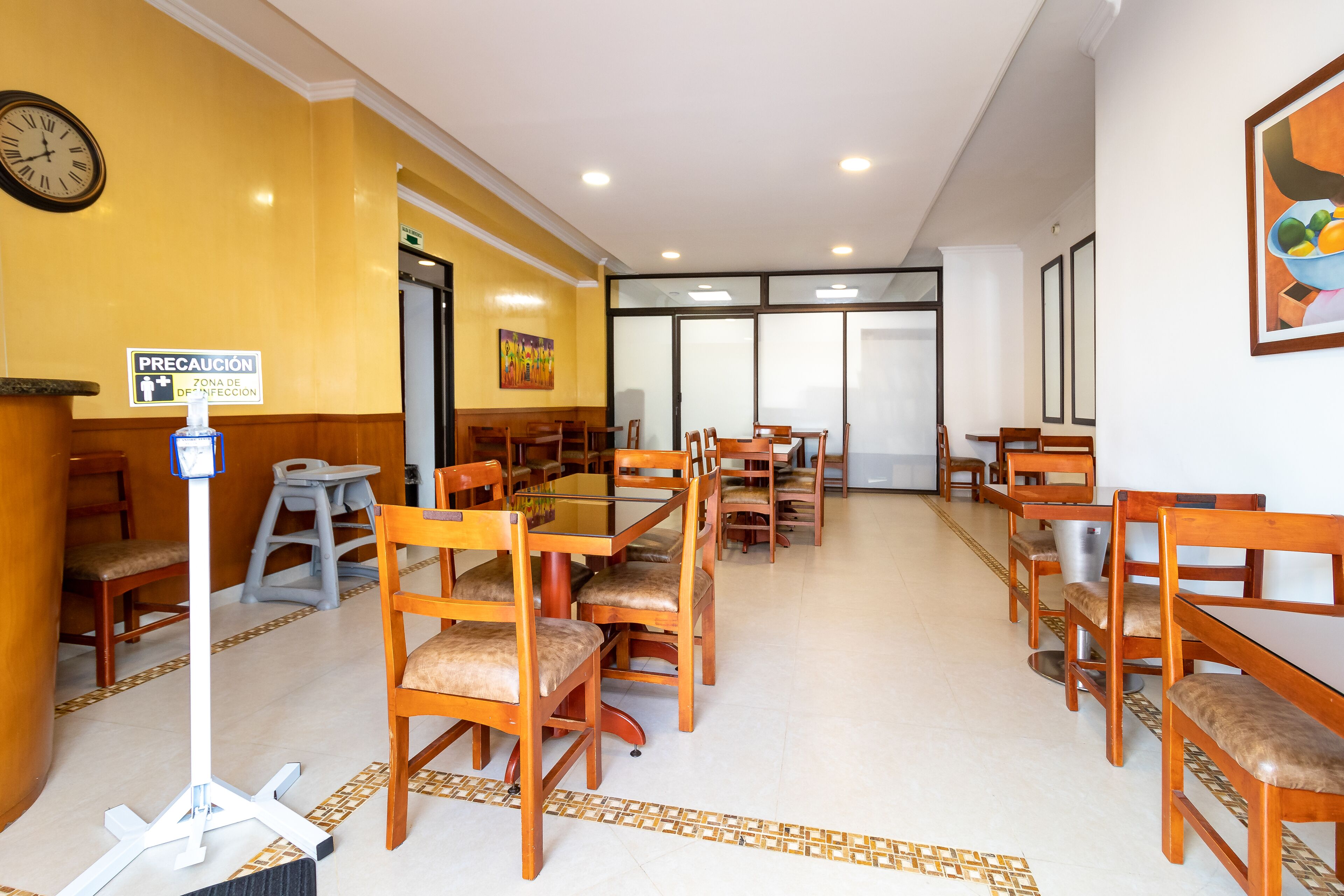 A dining area with wooden tables and chairs, a clock on the wall, and a caution sign.