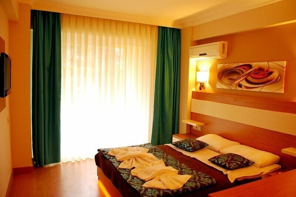 A hotel room with a bed, a TV, a painting, and a window with curtains.
