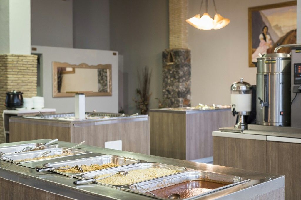 Zona de bufé con varias estaciones de servicio de alimentos, una máquina de café y una pared decorativa con espejo y obras de arte.