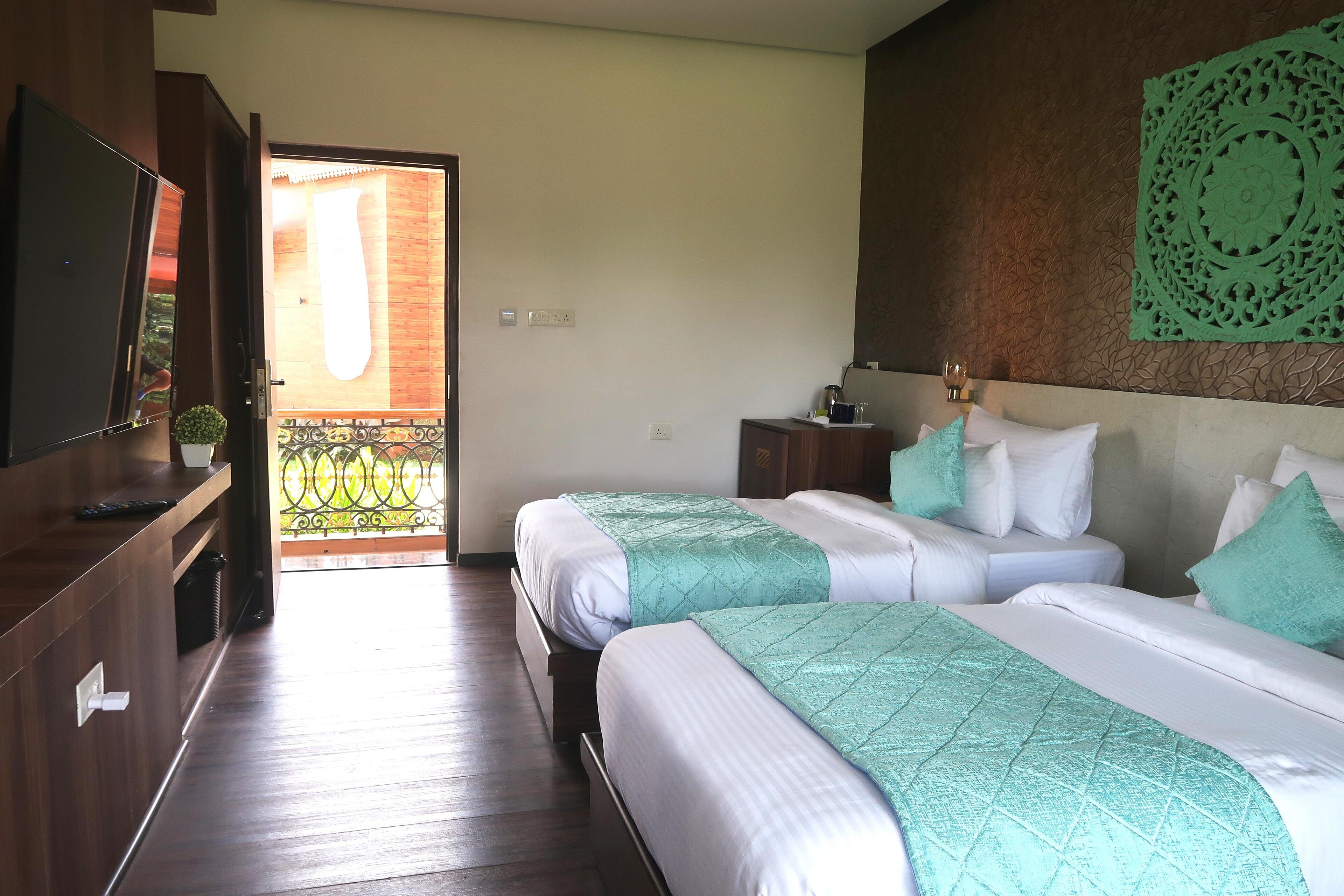 Quarto de hotel com duas camas, televisão, uma mesinha e um objeto decorativo na parede.