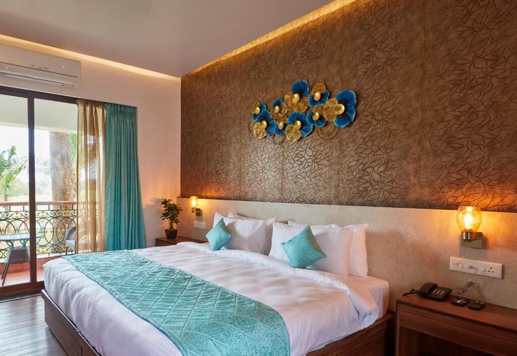 Quarto de hotel com cama, mesa de cabeceira, luminária na parede e vista para o exterior.