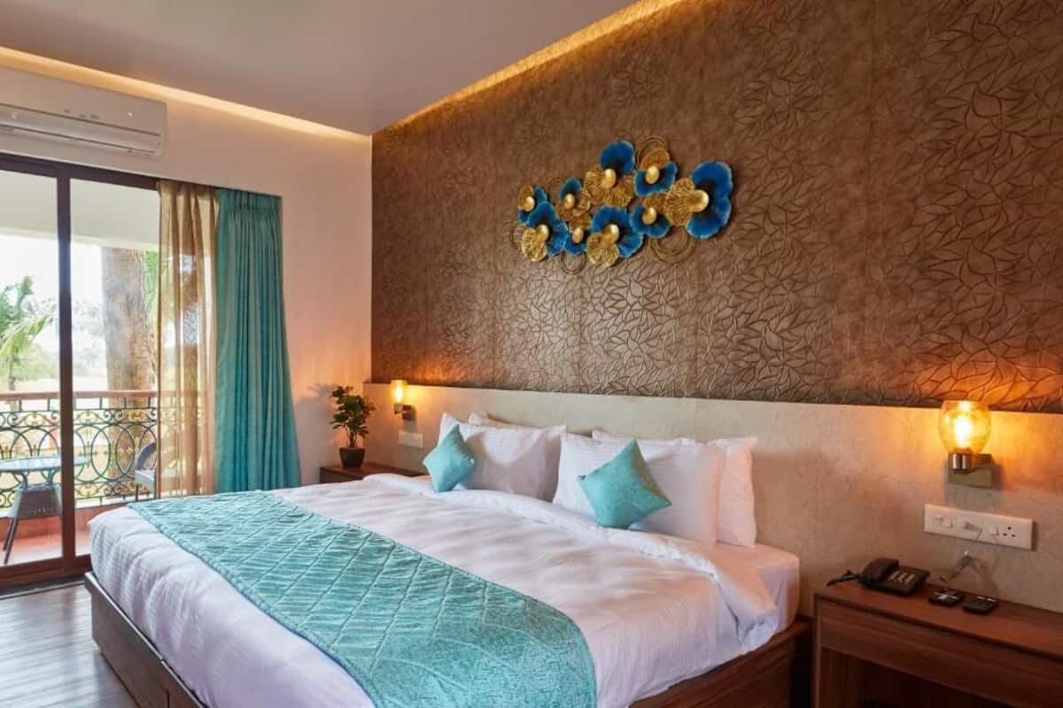 Quarto de hotel com cama, mesa de cabeceira, luminária na parede e vista para o exterior.