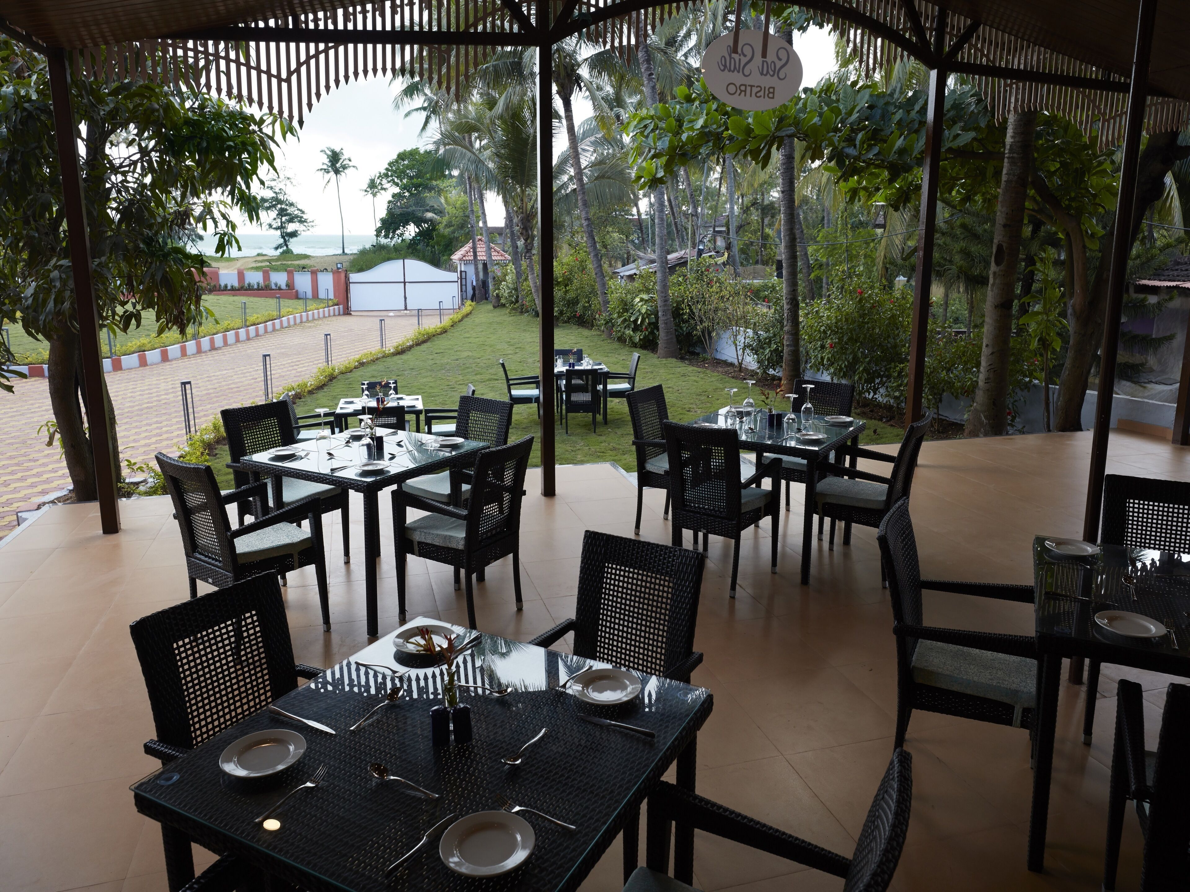 An outdoor dining area with tables and chairs, a view of the beach, and a sign reading "Sea Side Bistro".