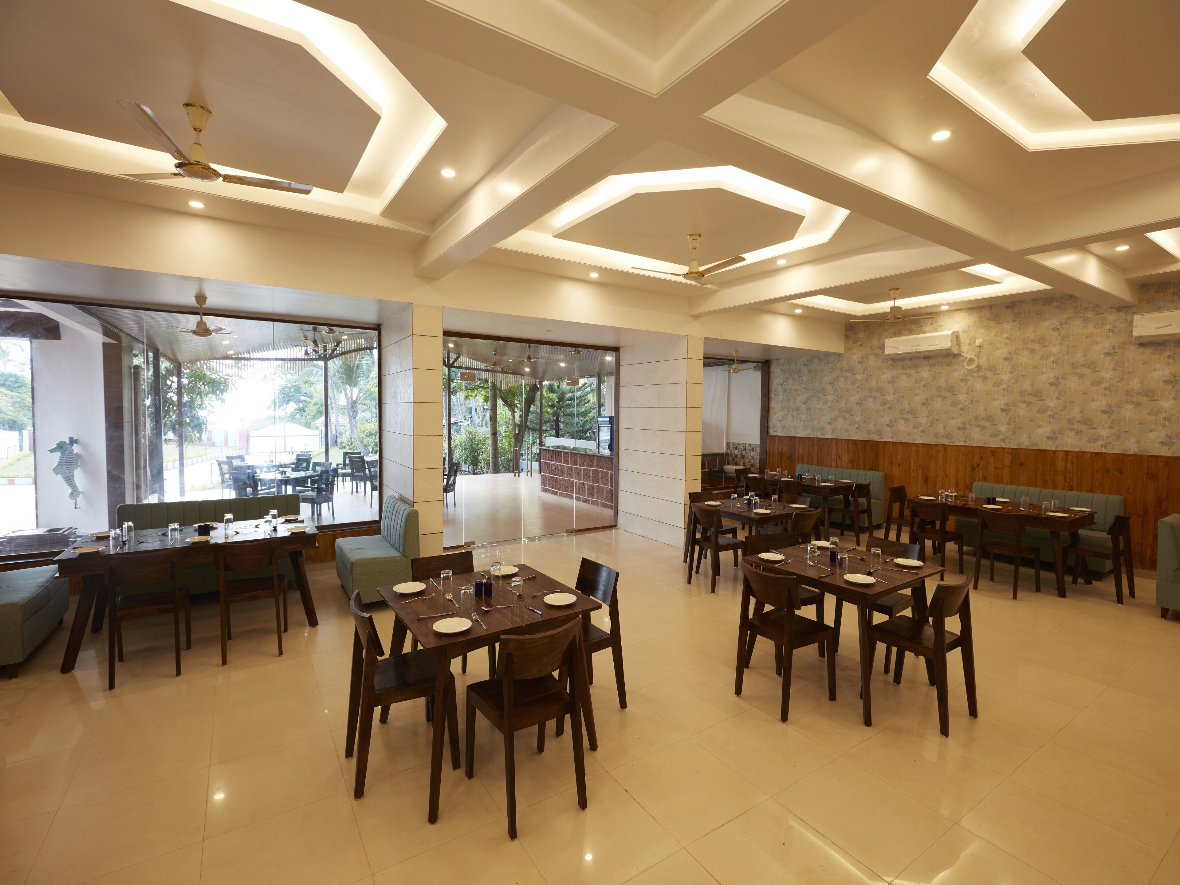 A spacious dining area with multiple tables and chairs, large windows offering views of the outdoors, and a modern ceiling design.