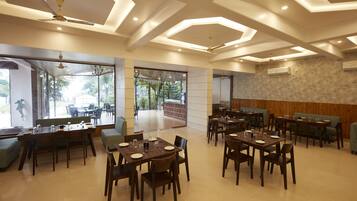 A spacious dining area with multiple tables and chairs, large windows offering views of the outdoors, and a modern ceiling design.