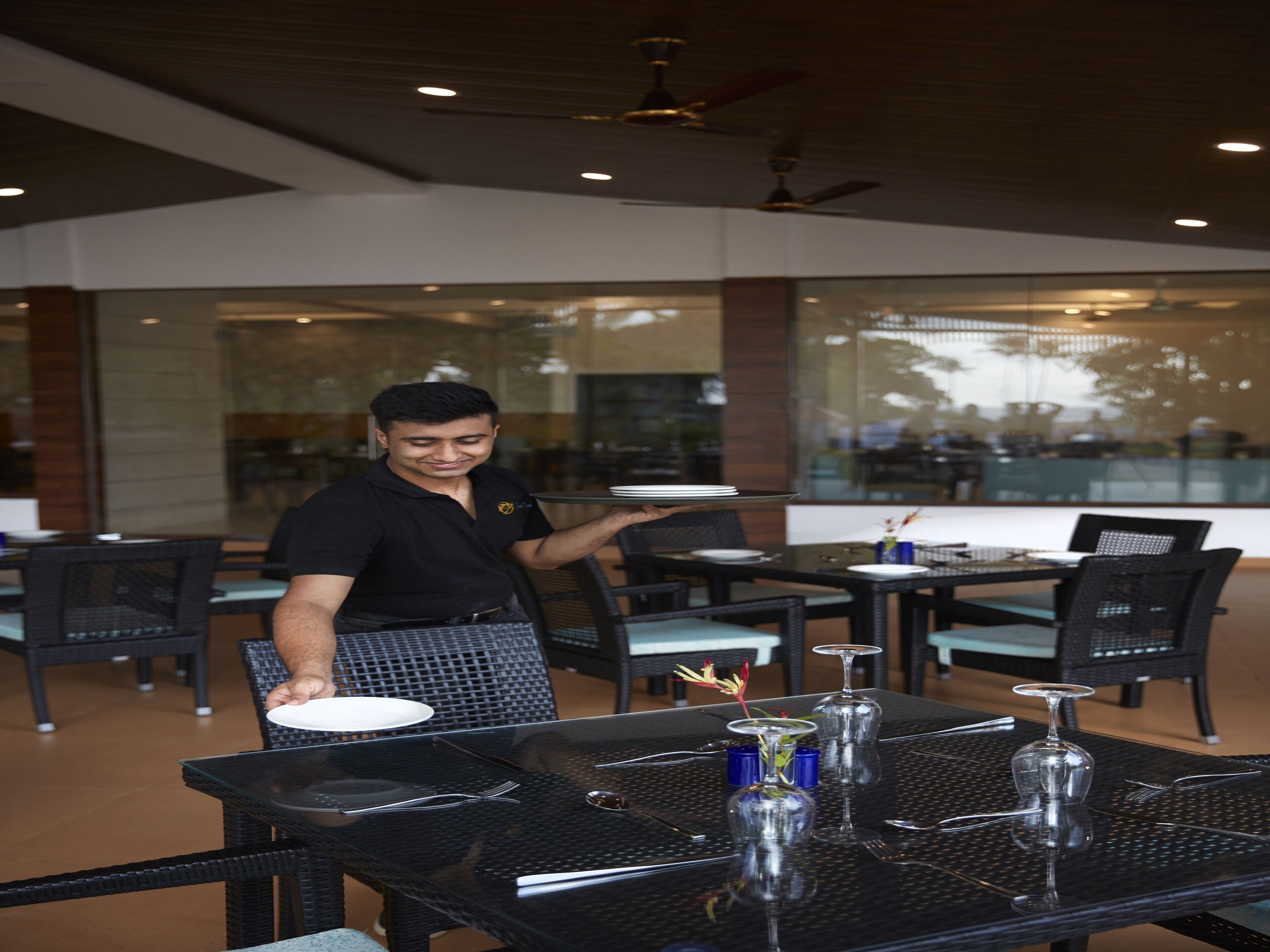 A restaurant with outdoor seating, including tables and chairs, and a waiter carrying a tray.