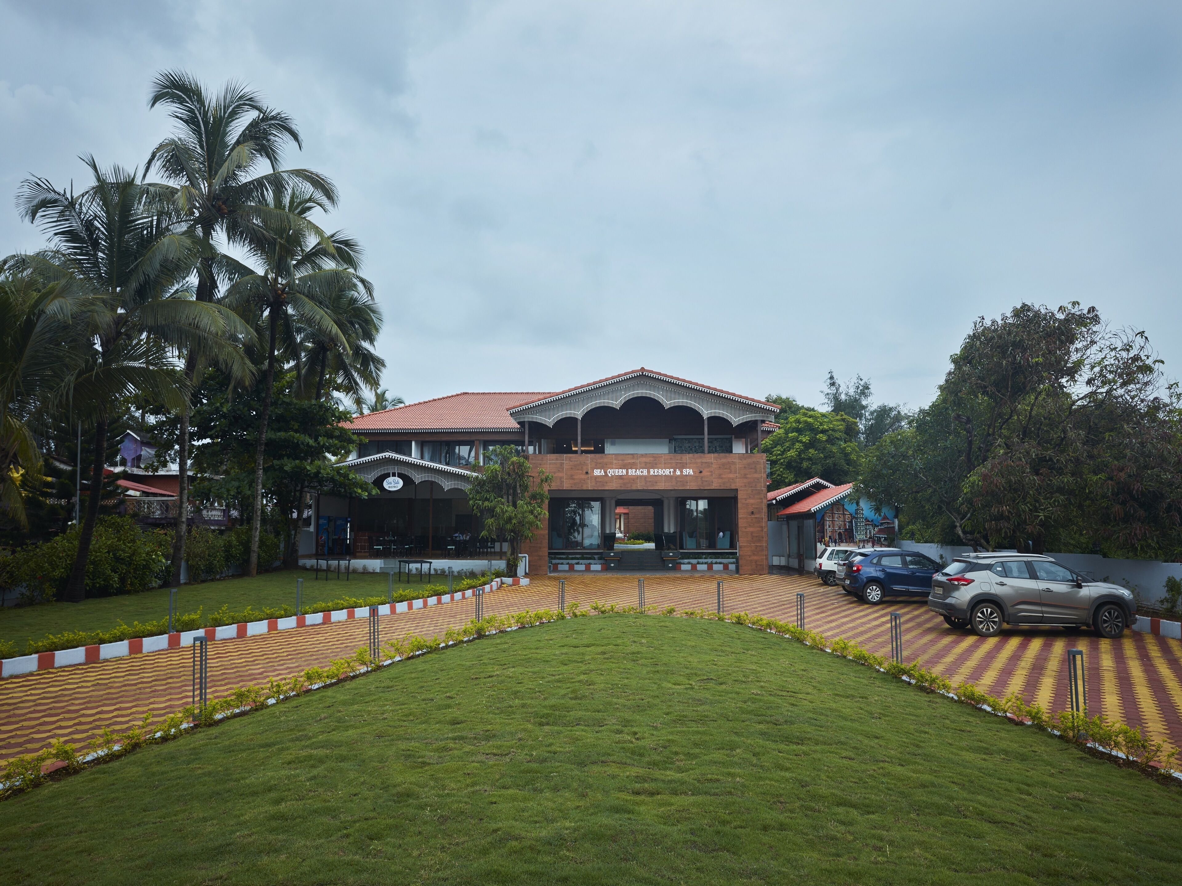 Un resort con un edificio central, palmeras y un estacionamiento.