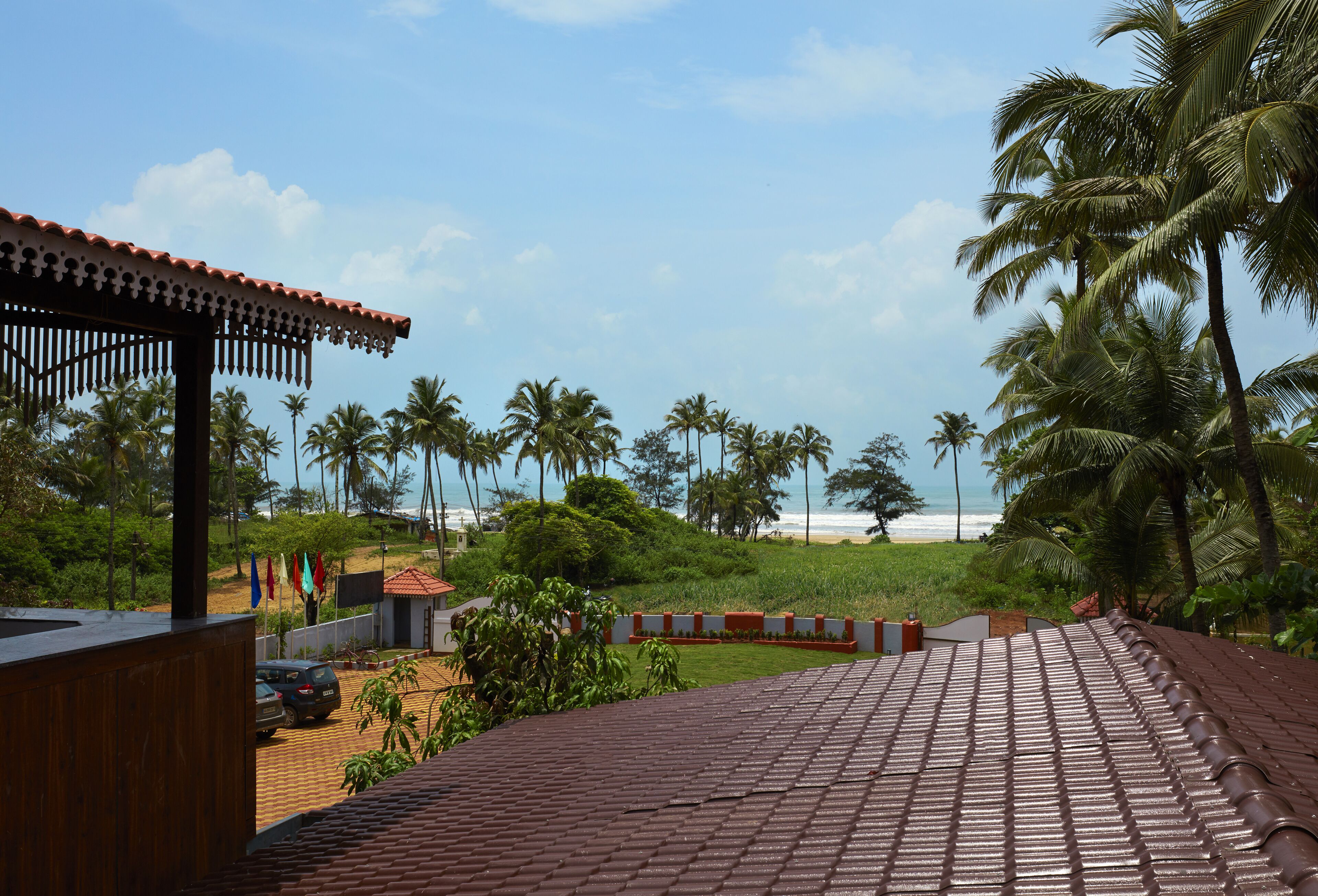 A coastal view with a tiled roof, palm trees, and a beach in the distance.