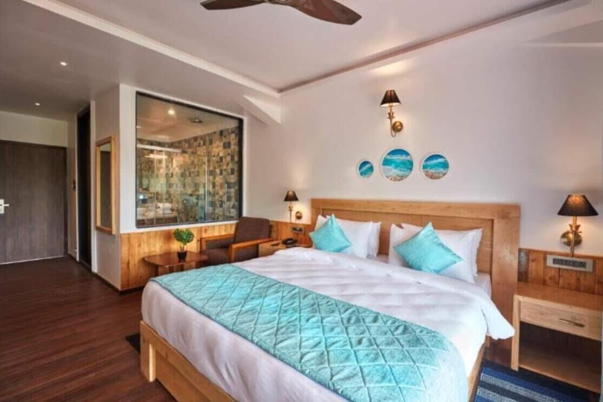 Quarto de hotel com uma cama grande, cabeceira de madeira, duas mesas de cabeceira, um criado-mudo e vista para o exterior.