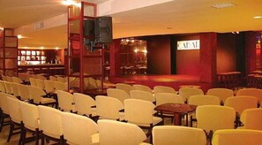 A theater with rows of chairs facing a stage, a bar area in the background, and a sign with the word 'CAFÉ' on the wall. - Club Cala Romani (Manacor)
