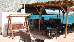 An outdoor seating area with wicker furniture, a swing, and a bar with bottles. - Elounda Sunrise Apartments (Agios Nikolaos)