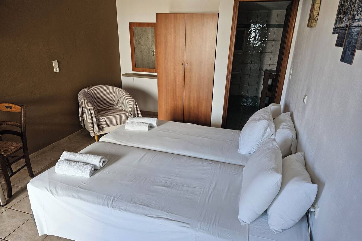 A hotel room with two beds, a wooden wardrobe, a chair, and a tiled floor.