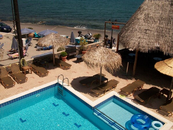 A pool area with lounge chairs and umbrellas, a thatched-roof structure, and a view of the sea.