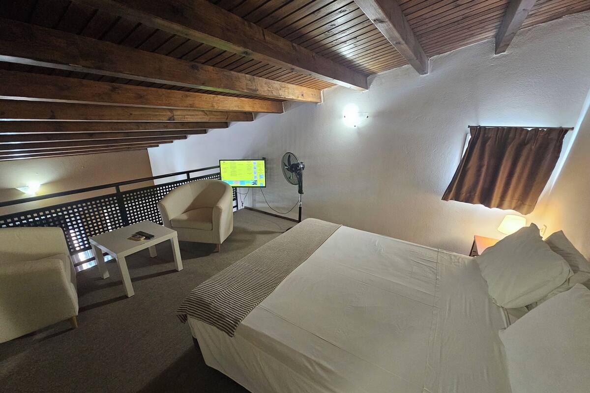 A hotel room with a bed, a desk, a chair, a TV, and a fan.