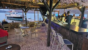 A restaurant with outdoor seating overlooking a body of water, a bar area, and a view of a boat. - Elounda Sunrise Apartments (Agios Nikolaos)