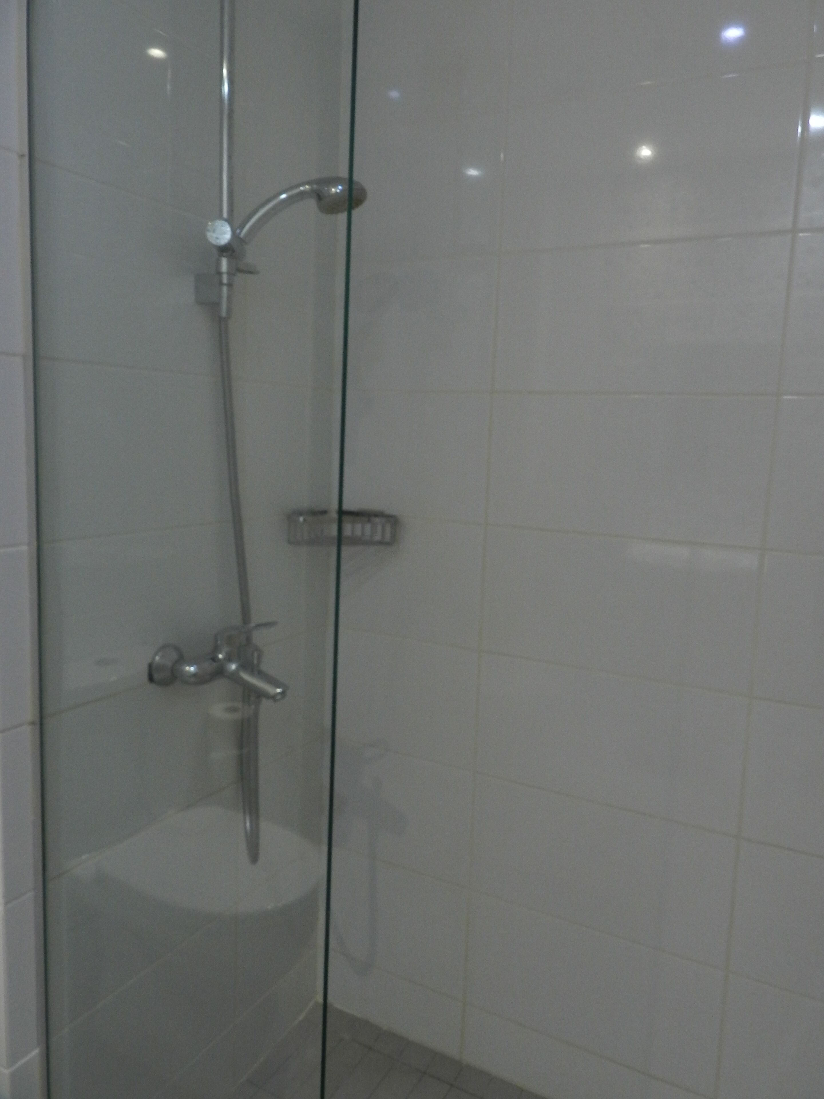 A glass-enclosed shower with a handheld showerhead and a wall-mounted faucet.