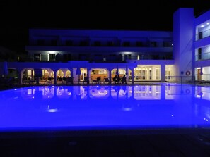 A pool with a blue-lit edge, a building with multiple balconies, and outdoor seating areas.
