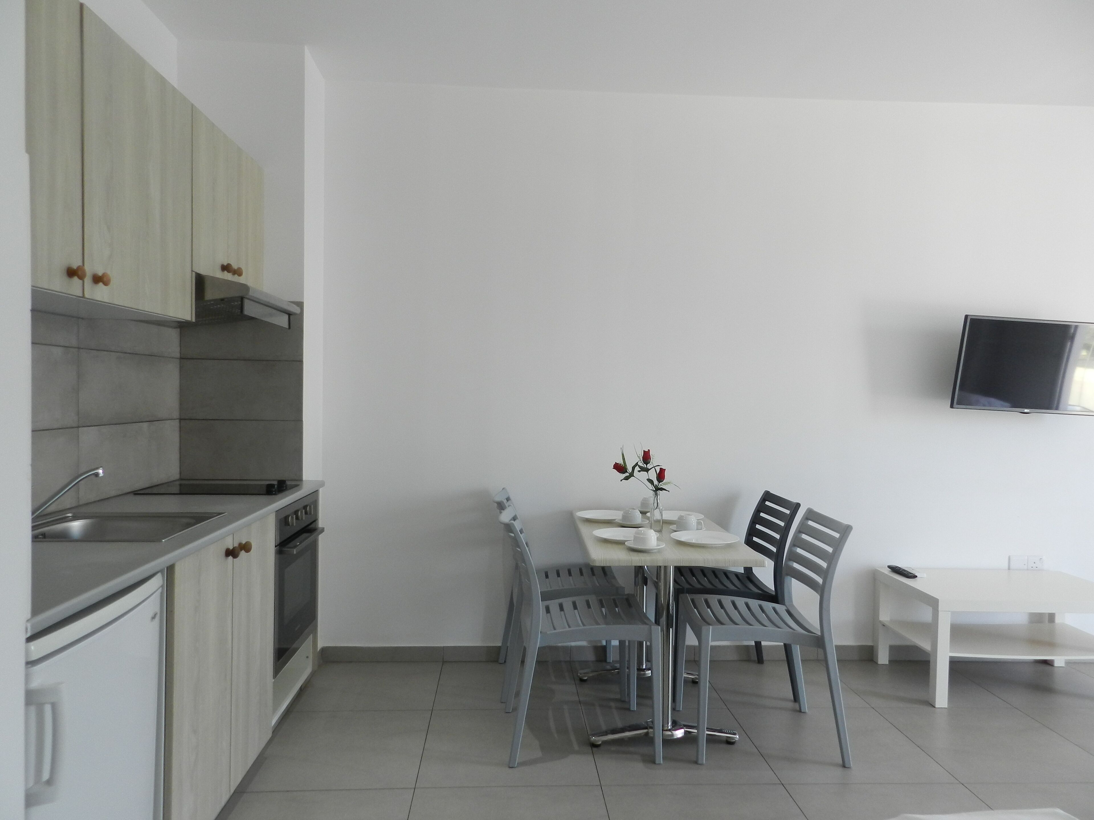 A modern kitchen with a dining area, including a table set for four, chairs, and a TV mounted on the wall.