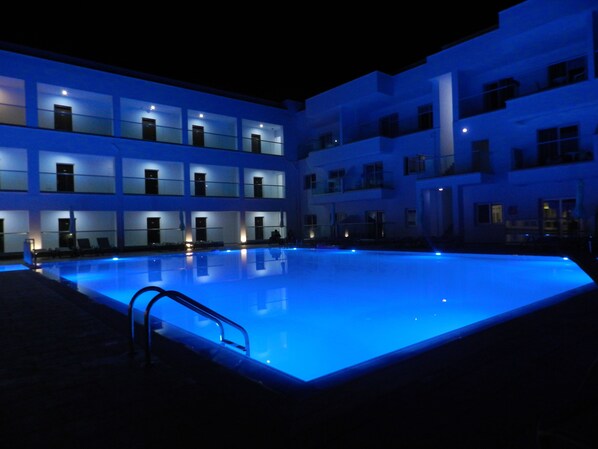 A multi-story hotel with a swimming pool at night, illuminated by blue lighting.