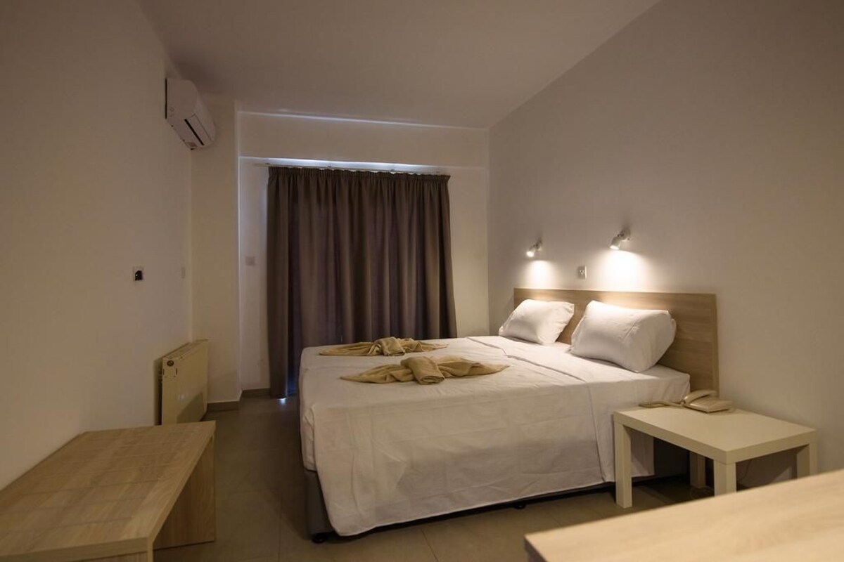A hotel room with a bed, bedside tables, a desk, and a window with curtains.