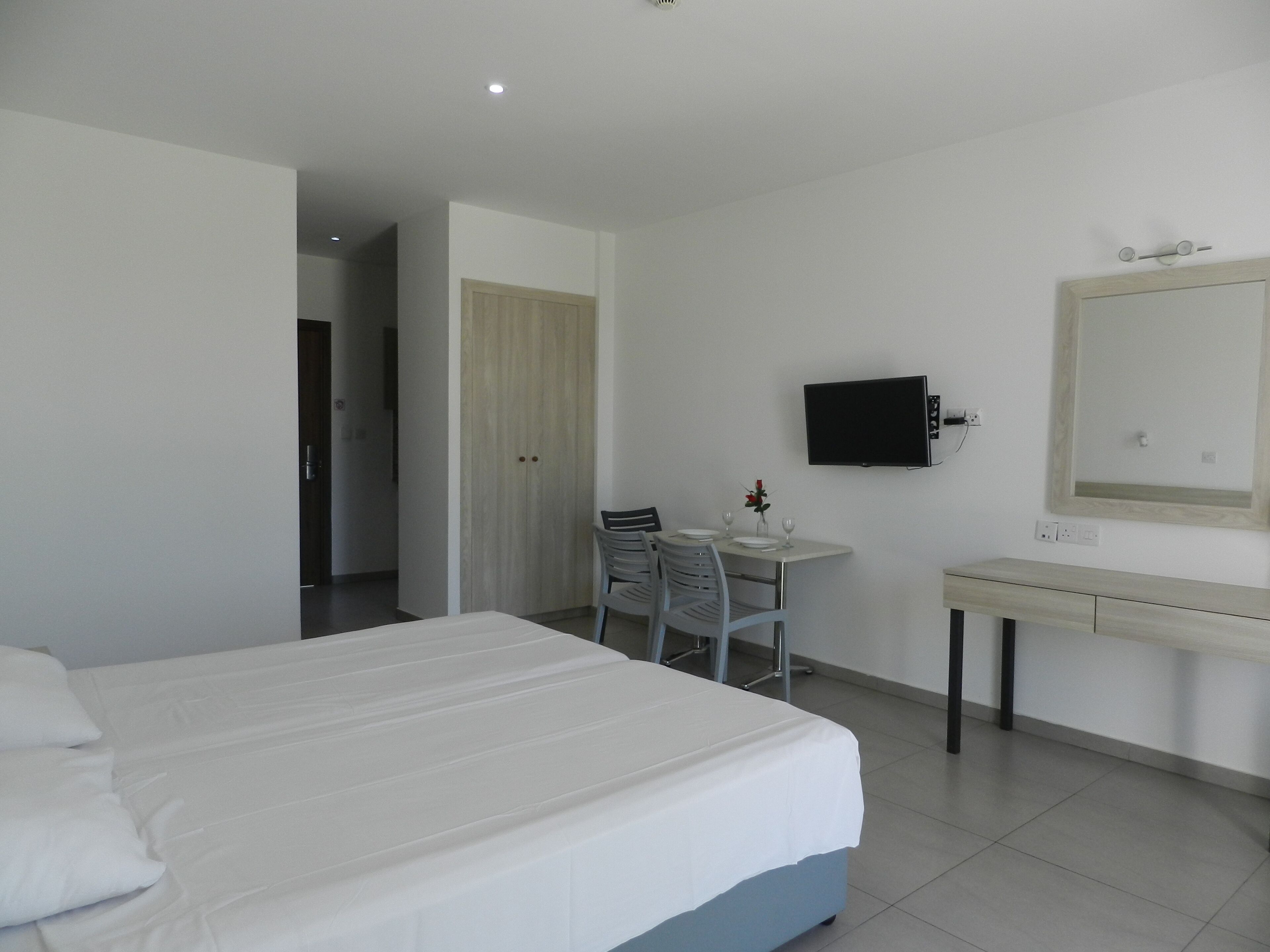 A hotel room with a bed, a desk, a chair, a television, and a mirror.