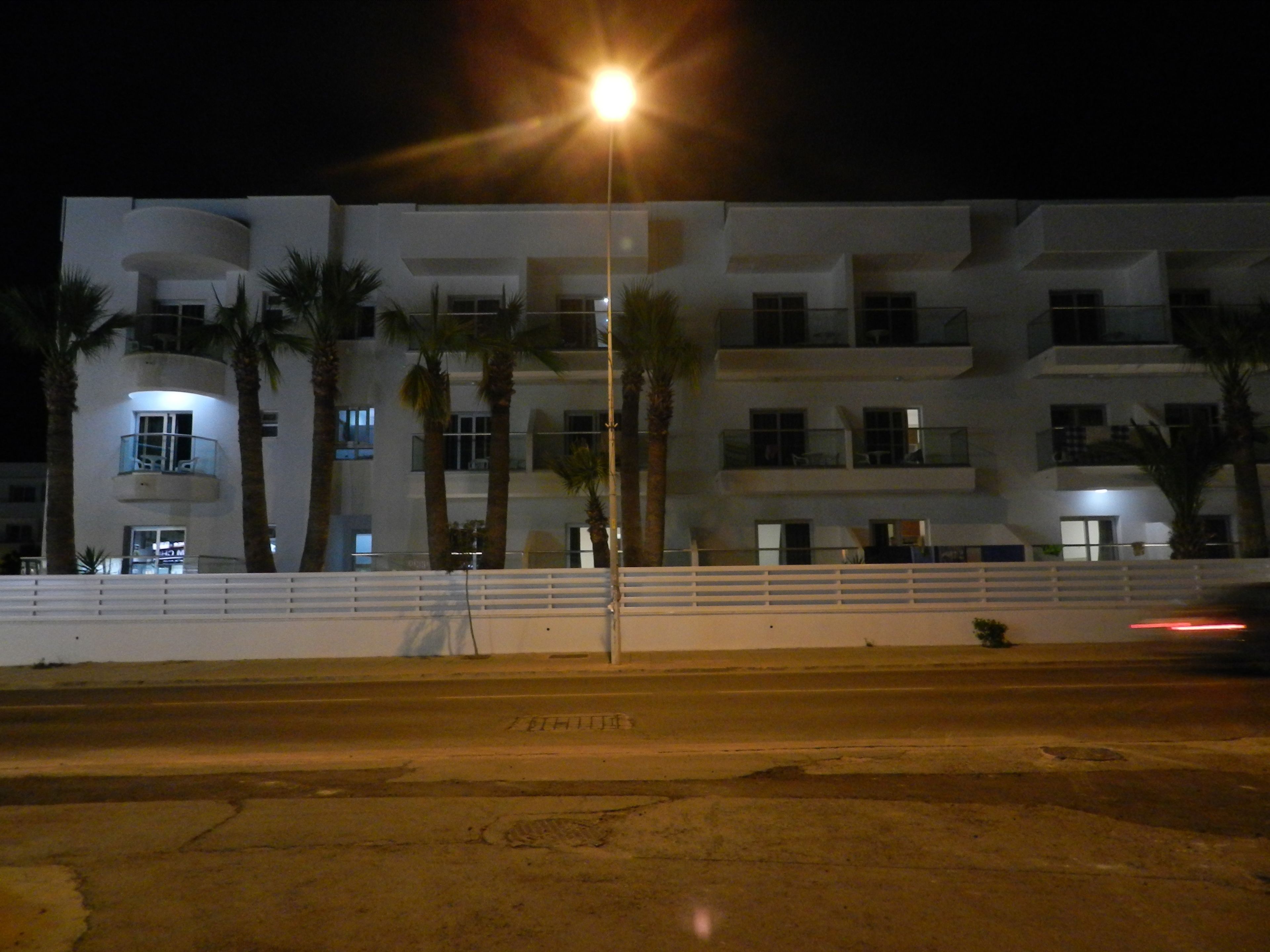 A multi-story building with balconies, palm trees, and a streetlight.