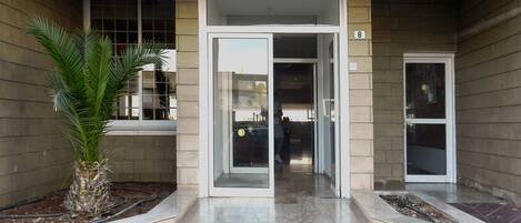 Entrada de un edificio con puerta de cristal, una palmera y el número '8' en la pared.