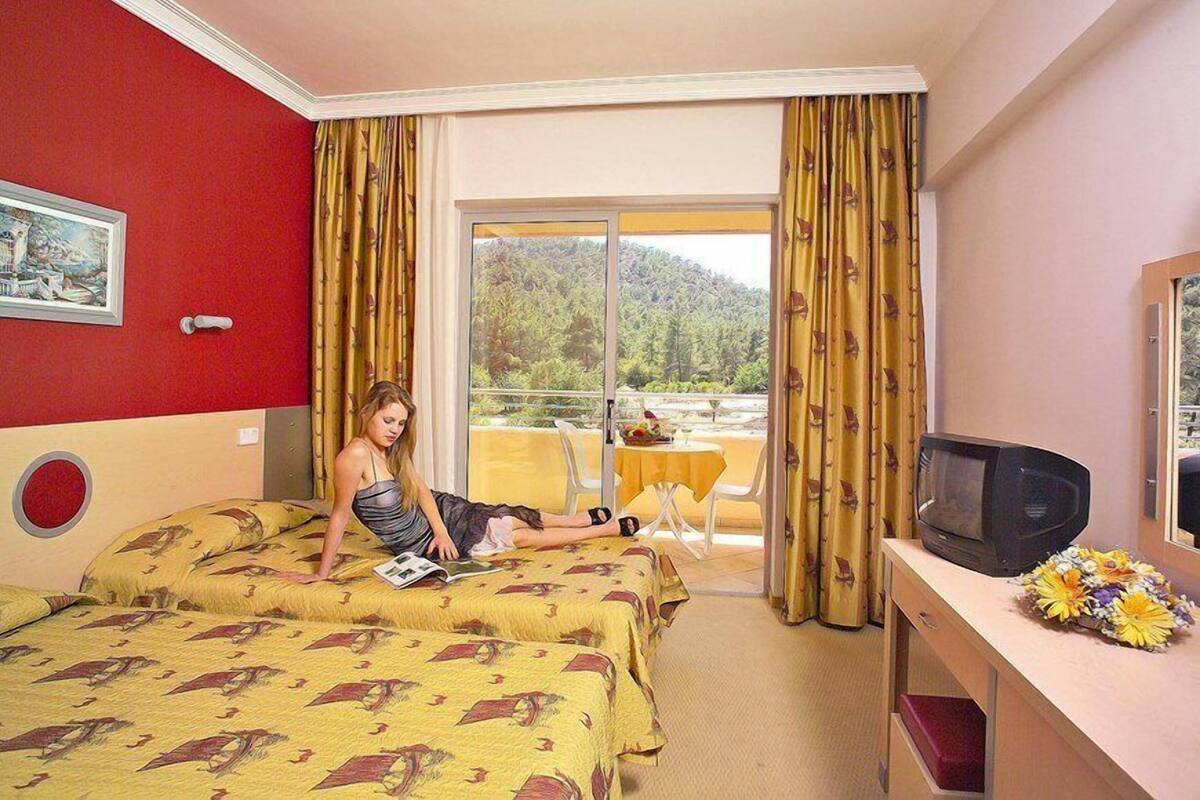 A hotel room with two beds, a TV, a balcony with a table, and a painting on the wall.