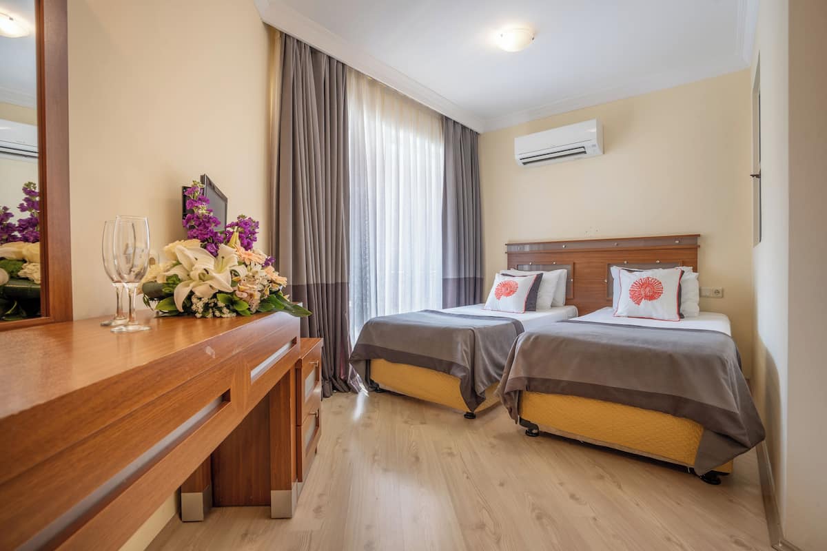A hotel room with two beds, a wooden desk, a mirror, and a large window with curtains.