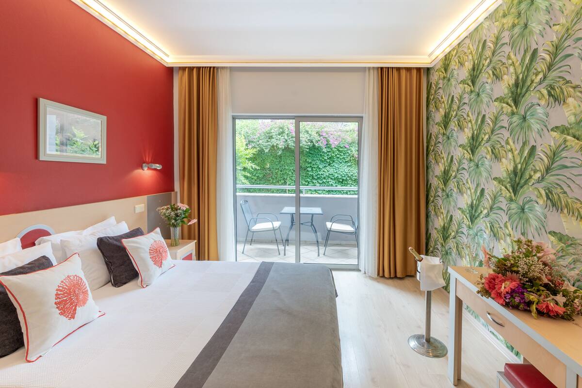 A hotel room with a large bed, a balcony with chairs, and a floral wall mural.