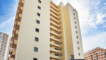 A multi-story hotel with a modern design, featuring a covered entrance and a parking area.