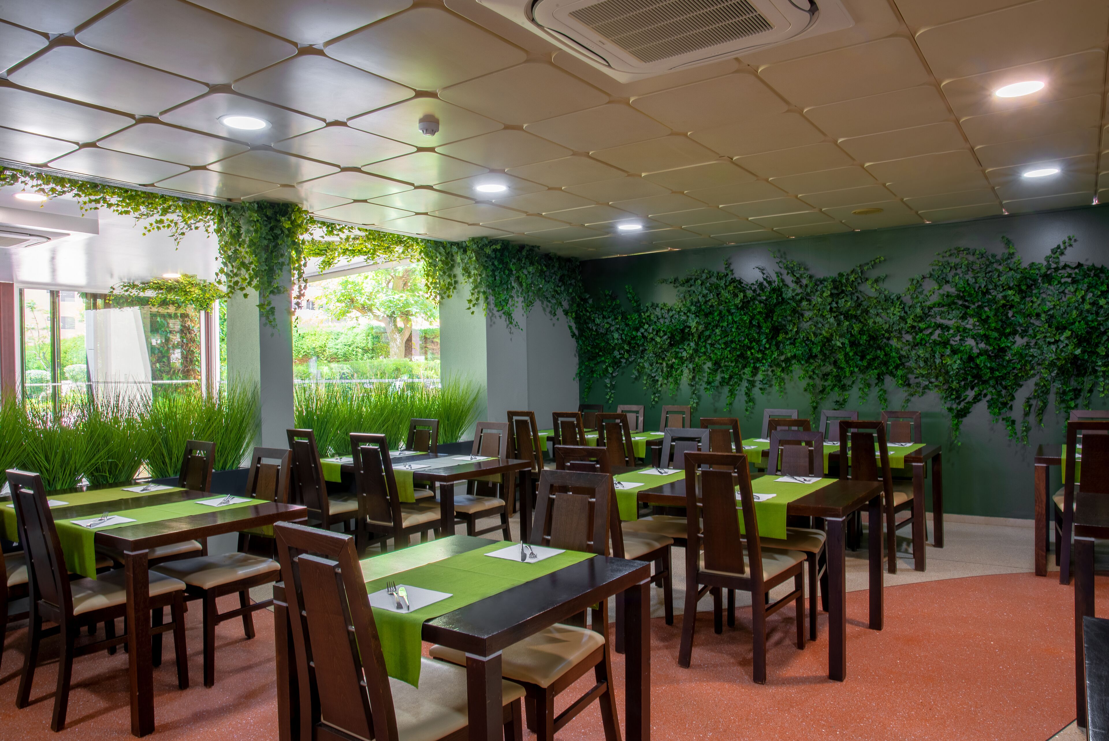 Sala de conferências com mesas e cadeiras, plantas verdes nas paredes e vista para o exterior com vegetação.