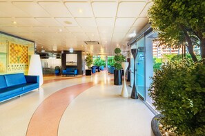 A modern lobby with a curved seating area, a reception desk, and a large window offering a view of greenery.