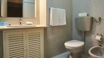 A bathroom with a toilet, bidet, sink, and mirror.