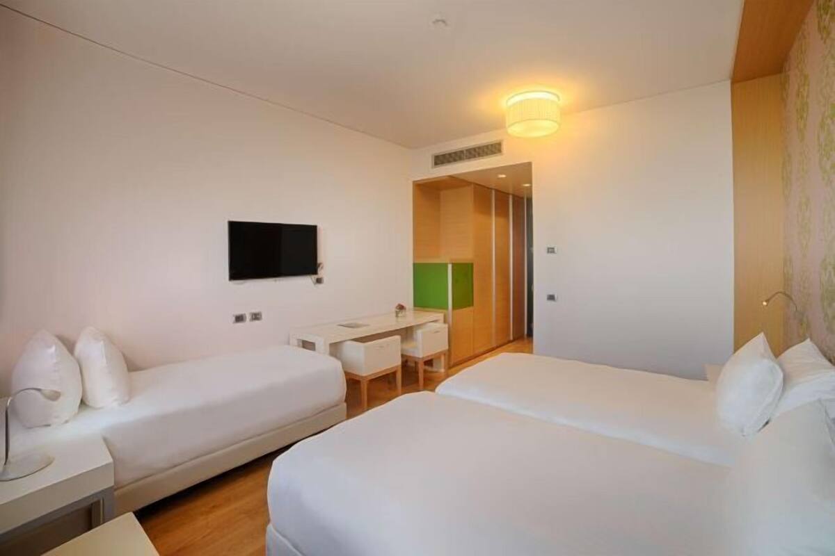 A hotel room with two beds, a desk, a chair, a TV, and a bathroom door.