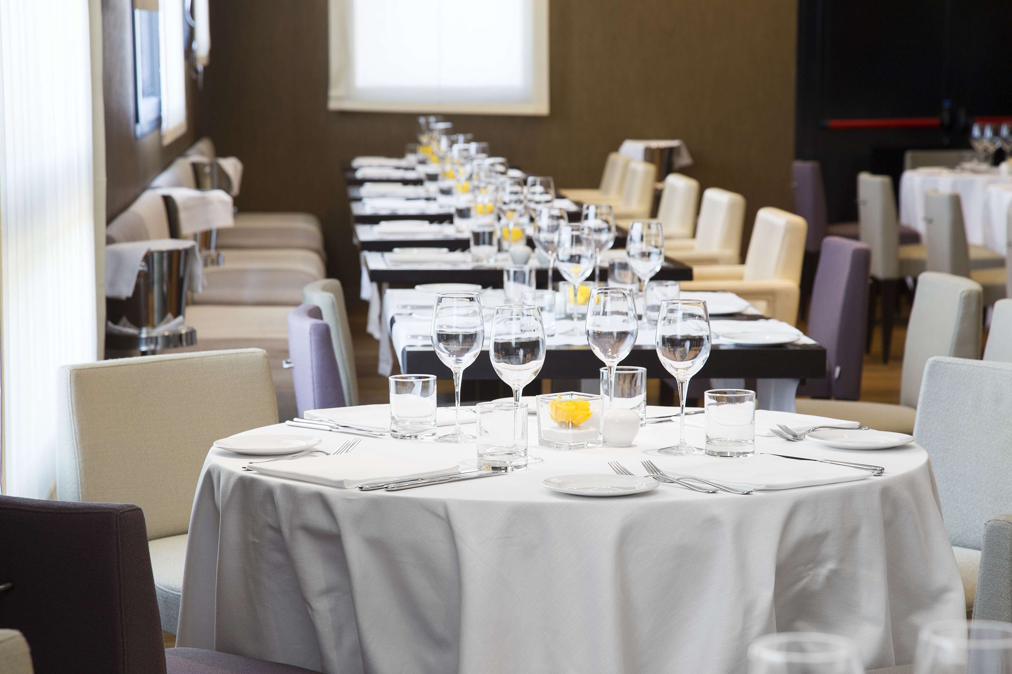 Una larga mesa dispuesta con manteles blancos, copas y cubiertos, que sugiere un comedor formal en un hotel.