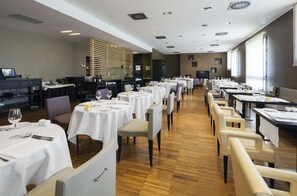 A spacious dining area with multiple tables set for guests, featuring a modern design with wooden flooring and neutral color tones.