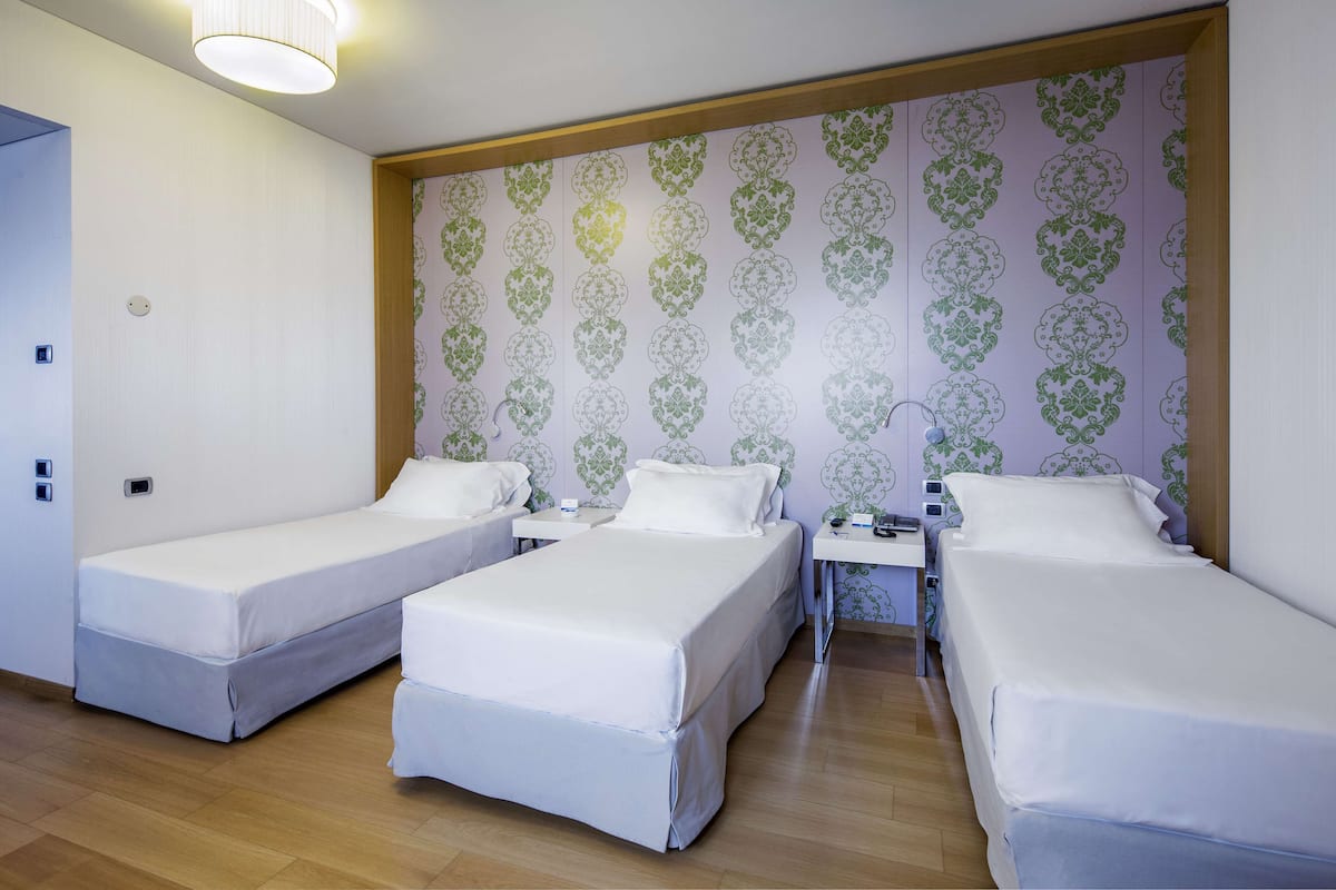 A hotel room with three single beds, a wooden ceiling, and a patterned wallpaper.