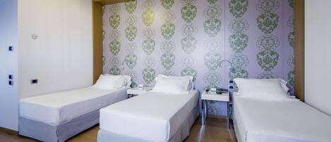 A hotel room with three single beds, a wooden ceiling, and a patterned wallpaper.