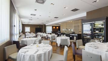A restaurant with round tables set for dining, a bar area with a wine cooler, and a modern ceiling design.