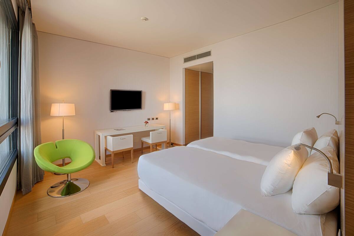 A hotel room with a bed, a desk, a chair, a TV, and a lamp.