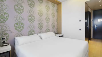 Habitación de hotel con una cama grande, una mesita de noche con lámpara y un papel tapiz estampado en la pared.