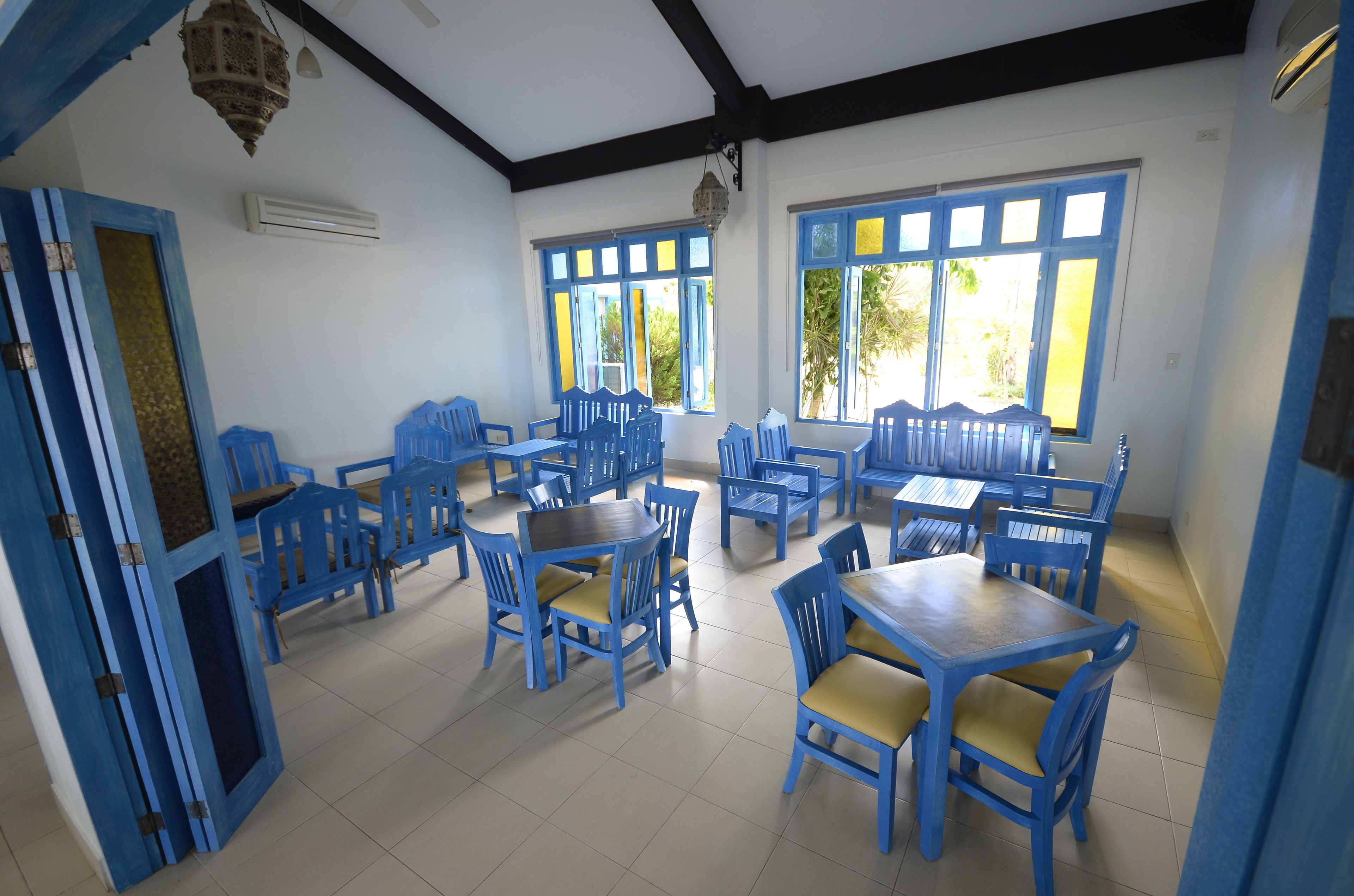A dining area with blue chairs and tables, large windows, and a ceiling fan.
